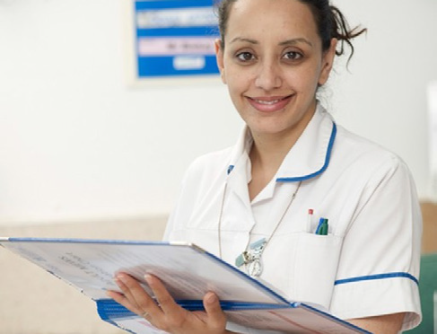 Figure 3. A nurse reading handwritten patient notes. Notes written in
                                poor handwriting can lead to patient fatalities.Source: "Smiling female
                                nurse on hospital ward with patient notes" is licensed under&nbsp;CC BY
                                4.0. 
